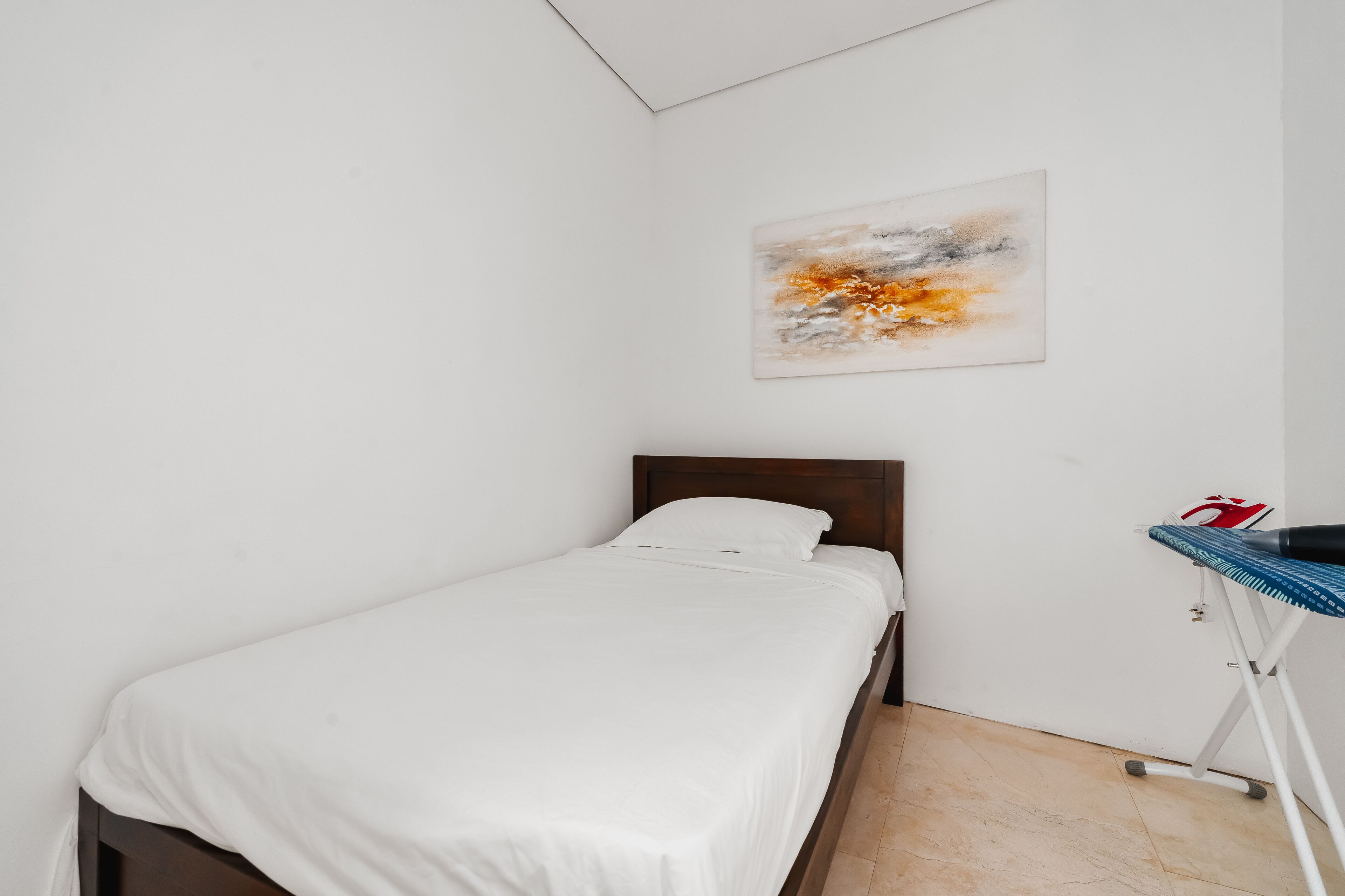 A single bed with a wooden headboard in a room with white walls and a tiled floor.