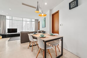 Un comedor moderno con una mesa preparada para cuatro personas, un sofá y un televisor al fondo.