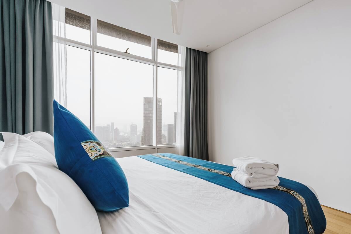 A hotel room with a bed, a window with curtains, a view of the city, and a neatly made bed with towels.