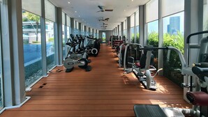 Una palestra con file di macchinari cardio e attrezzi per pesi, ampie finestre e una ventola a soffitto.