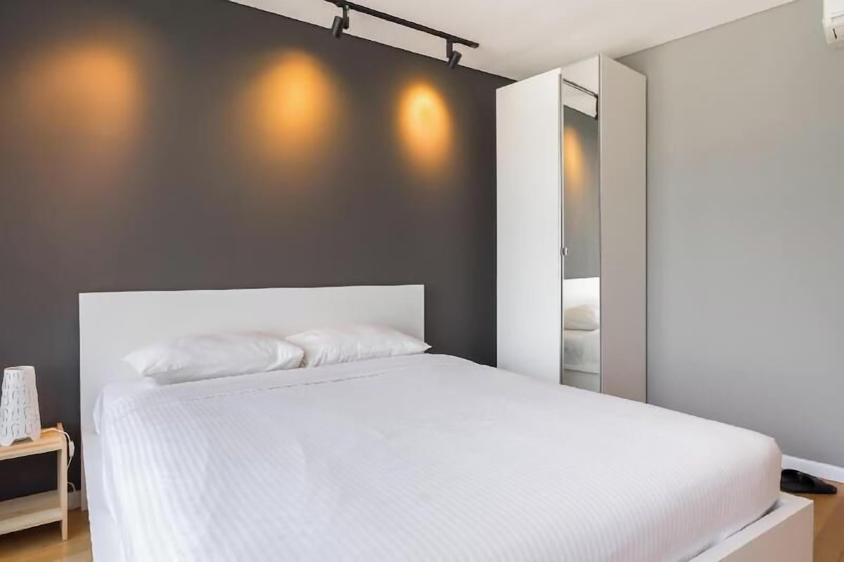 A modern bedroom with a large bed, a bedside table, and a wardrobe.