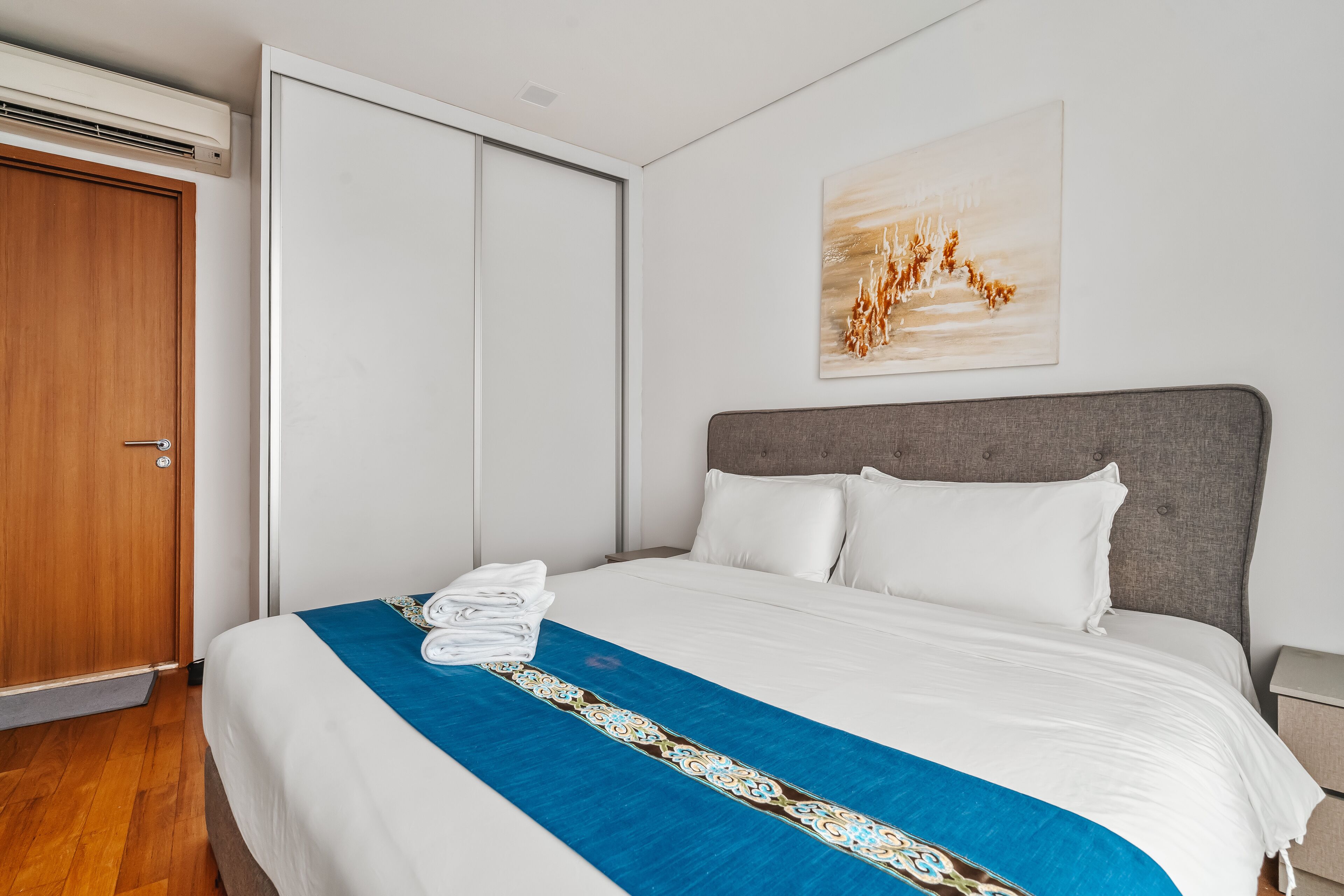 Une chambre d’hôtel avec un lit, une porte en bois, un mur blanc et un tableau.