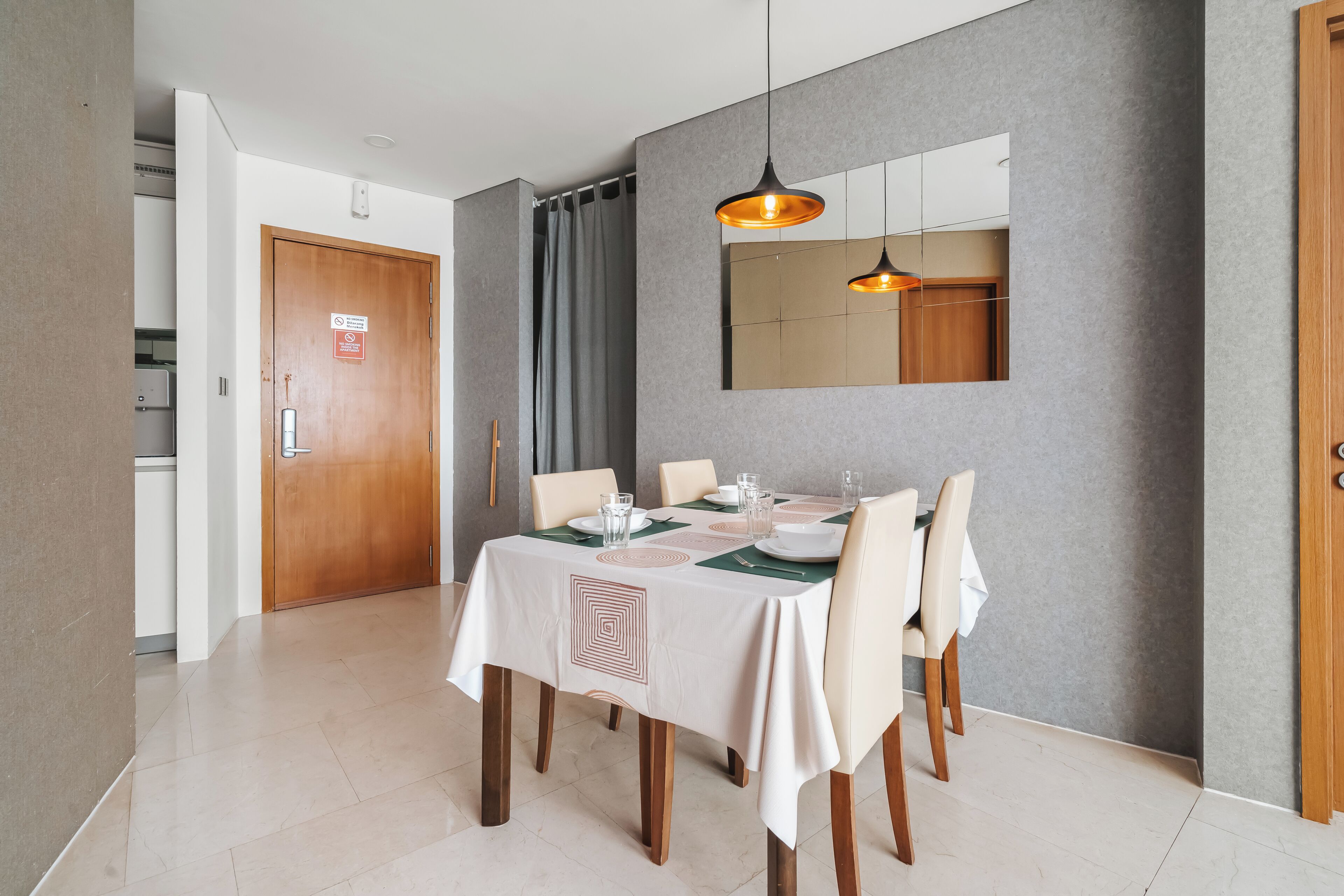 A dining area with a table set for four, a mirror above the table, and a door with a fire safety sign.