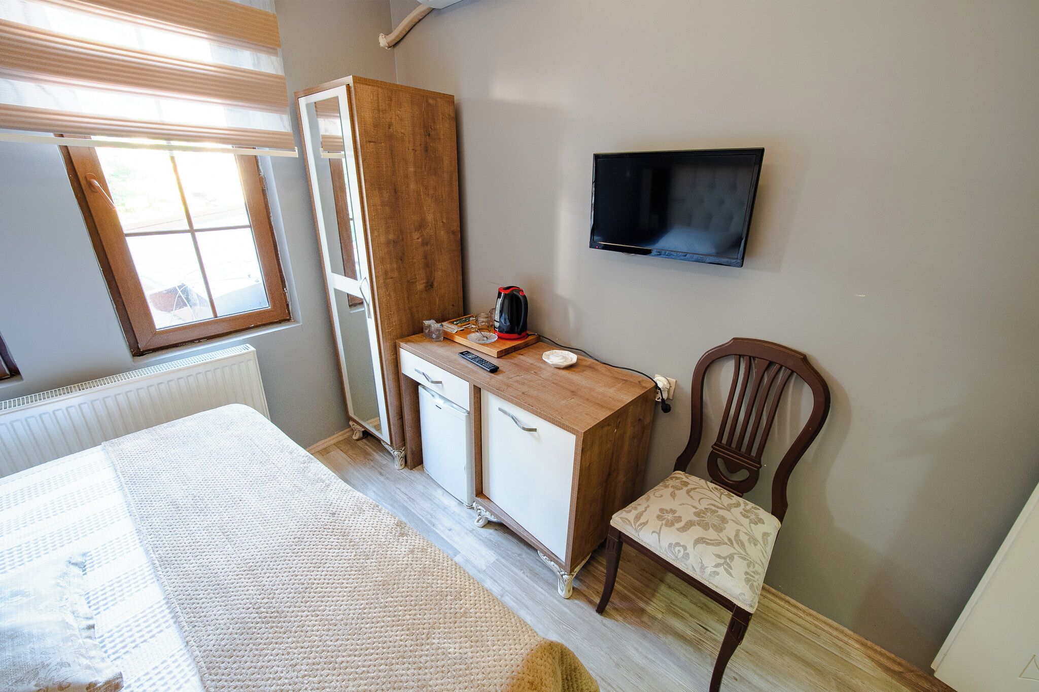 A bedroom with a bed, a wooden dresser, a chair, a television, and a window.