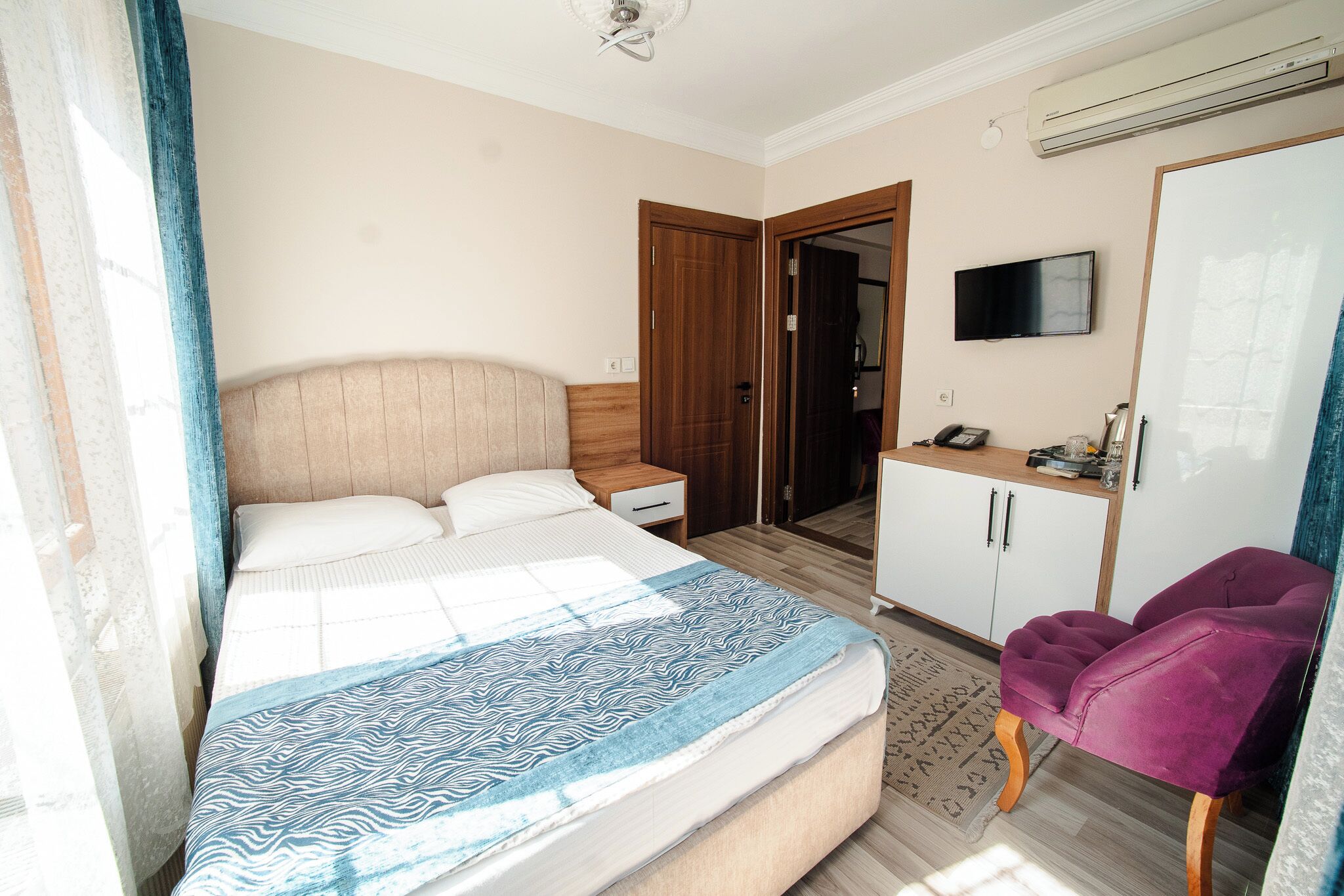 A bedroom with a bed, a wardrobe, a desk, a chair, and a TV.