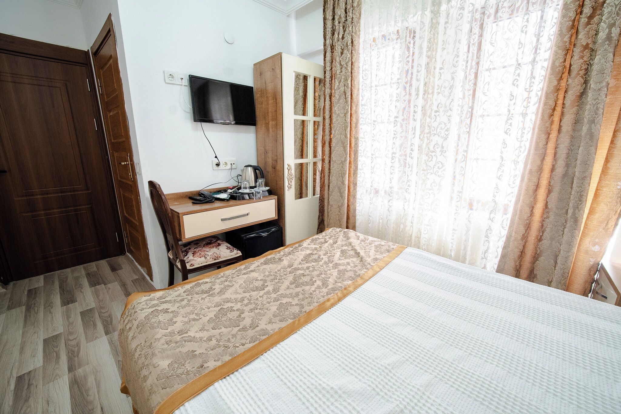 Un dormitorio con cama, escritorio, silla, armario y televisor en la pared.