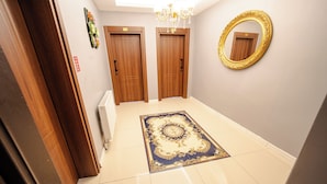 Un corridoio con due porte in legno, un lampadario e uno specchio al muro.