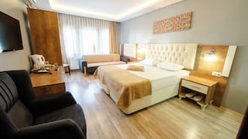 Habitación de hotel con cama, sofá, escritorio, televisor y piso de madera.