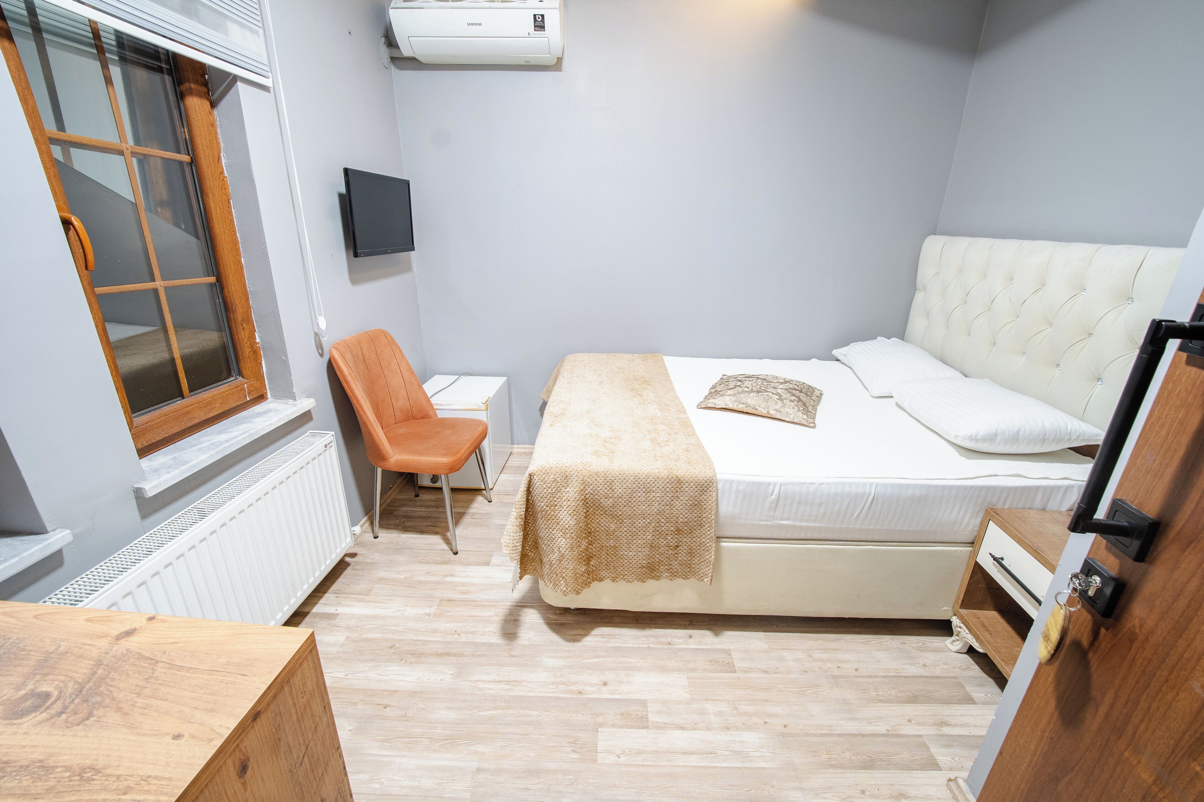 A bedroom with a bed, a chair, a TV, and a radiator.