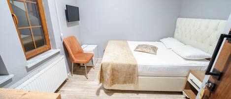 A bedroom with a bed, a chair, a TV, and a radiator.