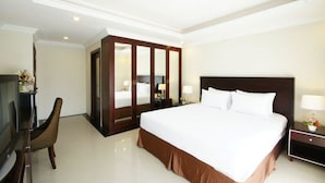 A hotel room with a large bed, a TV, a wardrobe, and a desk with a lamp.