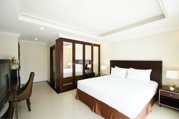 A hotel room with a large bed, a TV, a wardrobe, and a desk with a lamp.