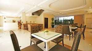 A spacious hotel lobby with a central dining area, a staircase, and a view of the outdoors.