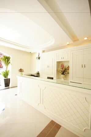 A modern kitchen with white cabinetry, a glass countertop, and decorative plants.