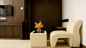 A modern living room with a flat-screen TV, a white side table with a vase of flowers, a cream-colored sofa, and dark wooden cabinets. - Imperial Regency (Kanayannur)