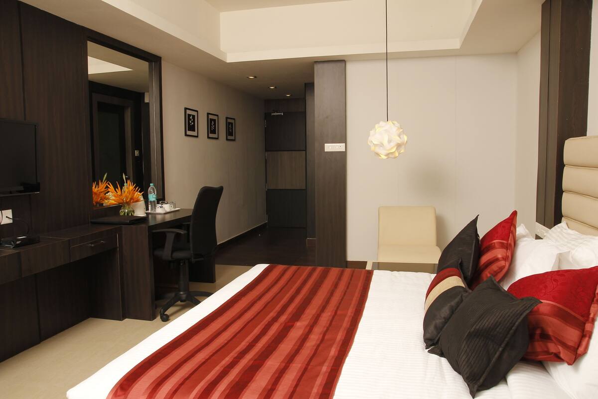 Una habitación de hotel con una cama grande, un escritorio, una silla, un televisor y un espejo.