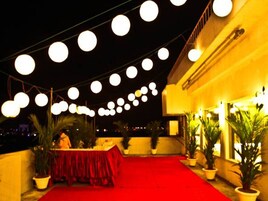 An outdoor area with a red carpet, potted plants, and string lights.