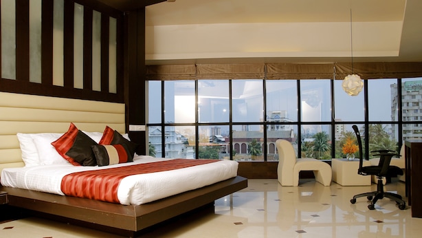 A modern hotel room with a large bed, a seating area, and a view of the cityscape through large windows. - Imperial Regency (Kanayannur)