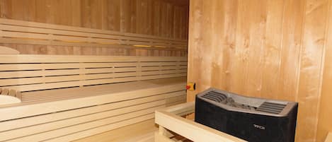 A sauna with wooden benches and a black sauna heater.