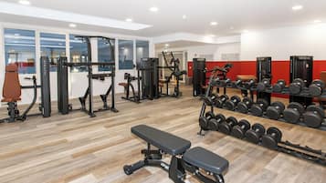 Un gimnasio con diferentes equipos de ejercicio, incluyendo máquinas de pesas y mancuernas, además de un banco.