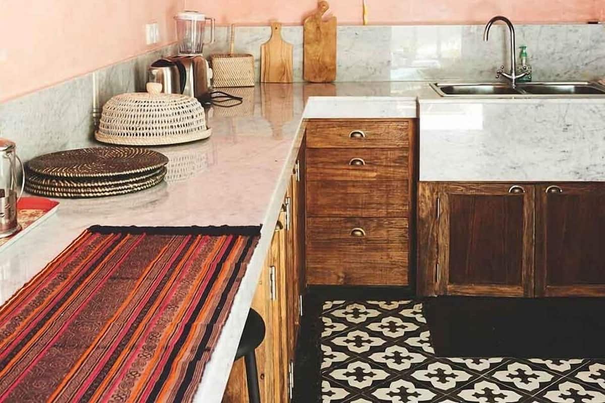 A kitchen with a pink wall, wooden cabinets, a marble countertop, and hanging pendant lights.