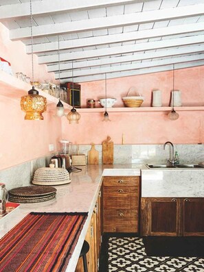 A kitchen with a pink wall, wooden cabinets, a marble countertop, and hanging pendant lights.