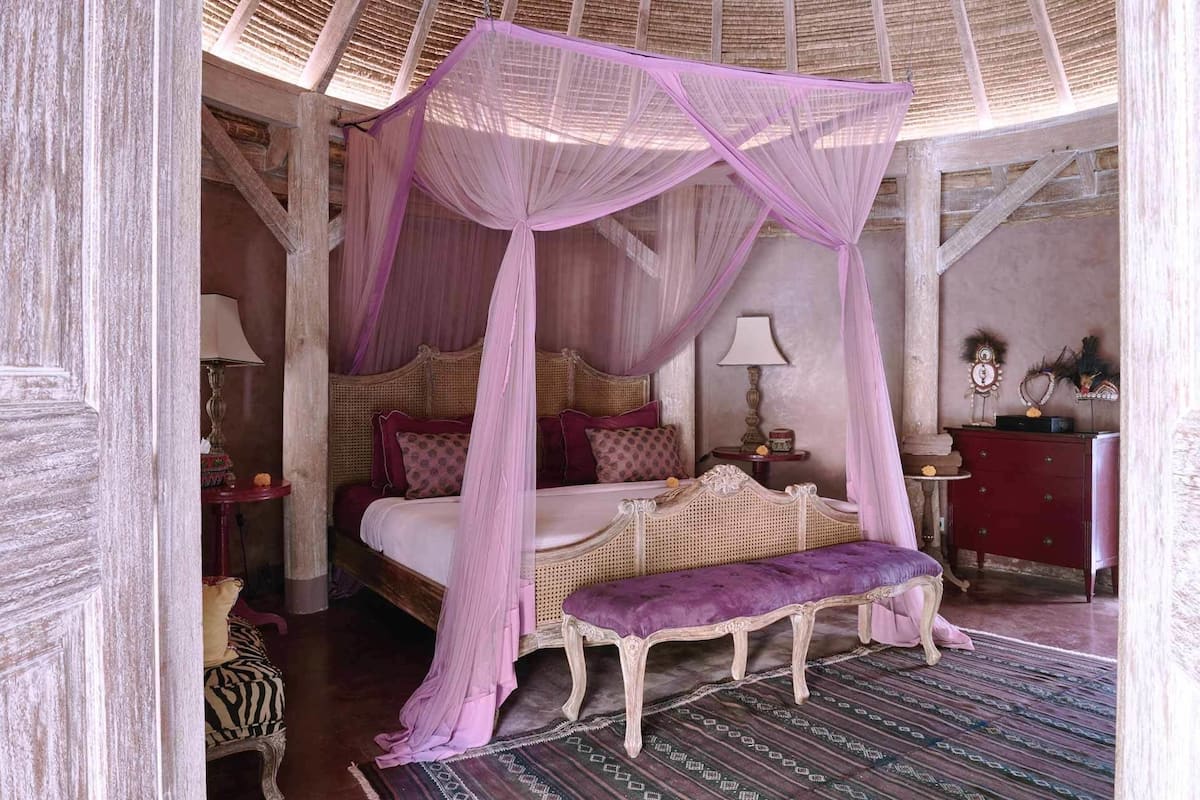 A room with a four-poster bed, a bench, a nightstand, and a lamp.