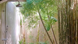 Een badkamer met een douche, omringd door bamboeplanten en een betonnen muur.