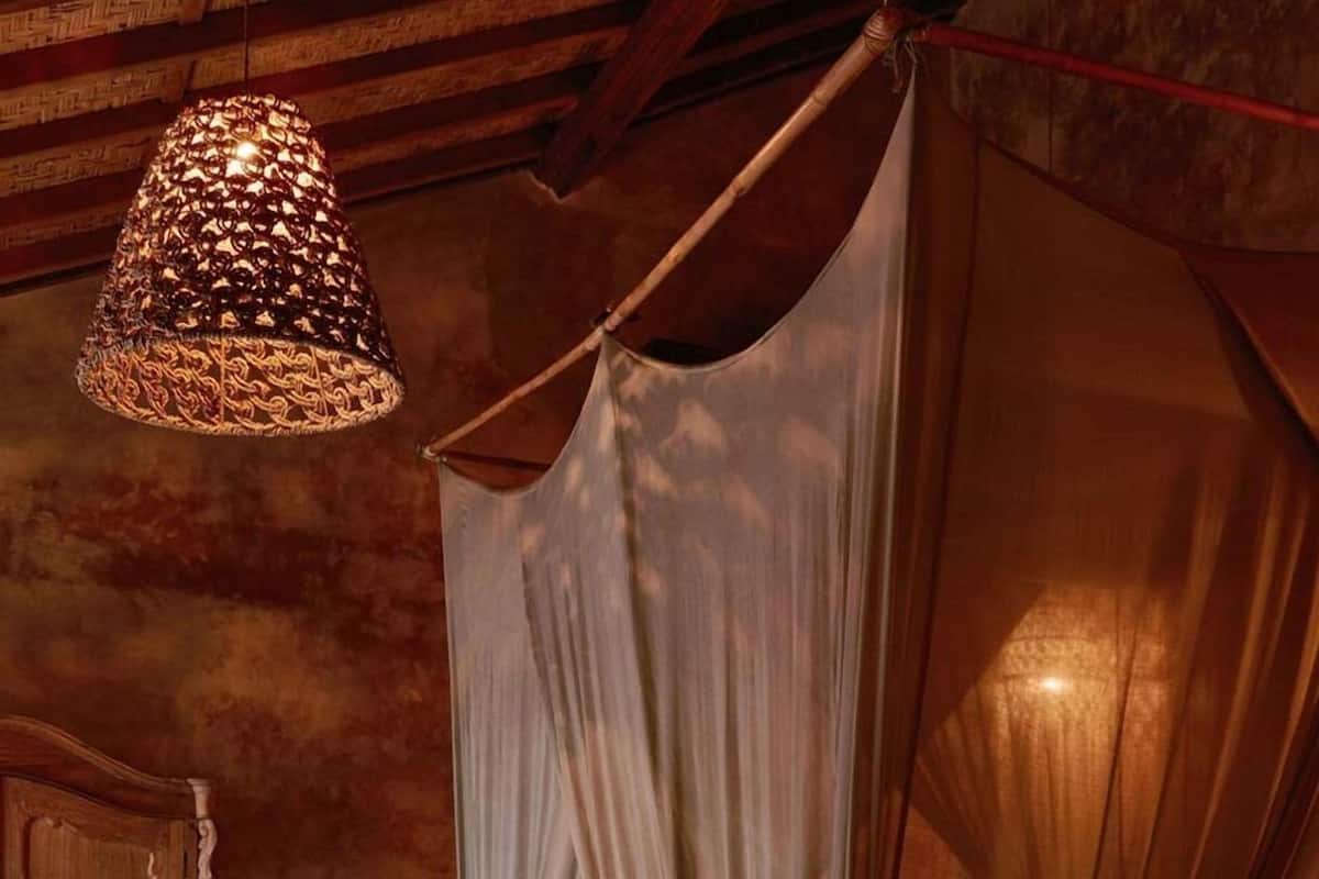 A four-poster bed with a canopy, a wooden wardrobe, and a hanging lamp.