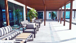 A covered outdoor seating area with sofas and tables, large windows, and potted plants. - Surgrand Hotel (Sur)