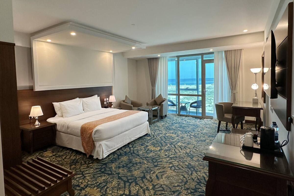 A hotel room with a bed, a desk, a chair, a TV, and a view of the ocean.