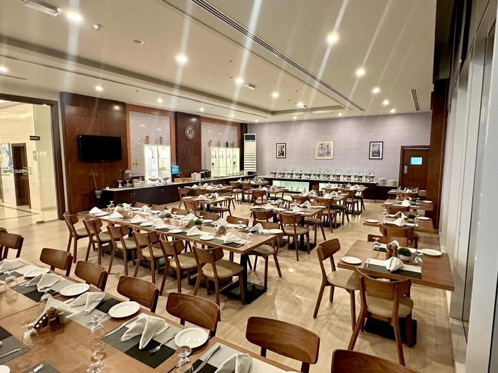 A spacious dining area with multiple tables and chairs, a long counter with a television, and a modern interior design.