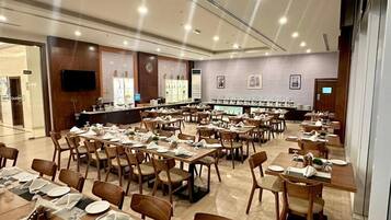 A spacious dining area with multiple tables and chairs, a long counter with a television, and a modern interior design.