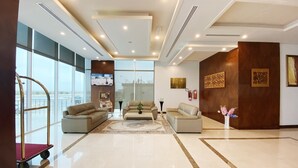 A spacious lobby with a large seating area, a television mounted on the wall, and a view of the outside through large windows. - Surgrand Hotel (Sur)
