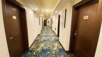 Een hotelgang met tapijtelkeerpatroon, houten deuren en genummerde deurbelplaten.