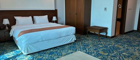 A hotel room with a large bed, a wooden wardrobe, a small table, and a seating area with chairs.