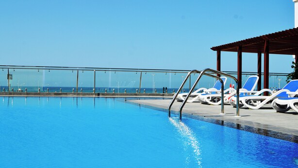 A clear blue pool with lounge chairs and a glass railing overlooking the ocean. - Surgrand Hotel (Sur)