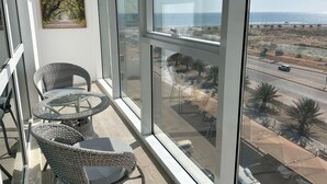 A balcony with wicker chairs and a table, a painting on the wall, and a view of a road and landscape. - Surgrand Hotel (Sur)