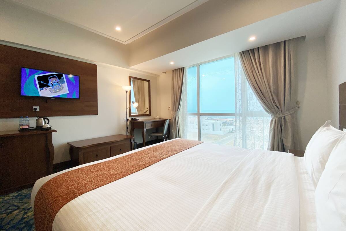 A hotel room with a large bed, a desk, a chair, a television, and a window with curtains.