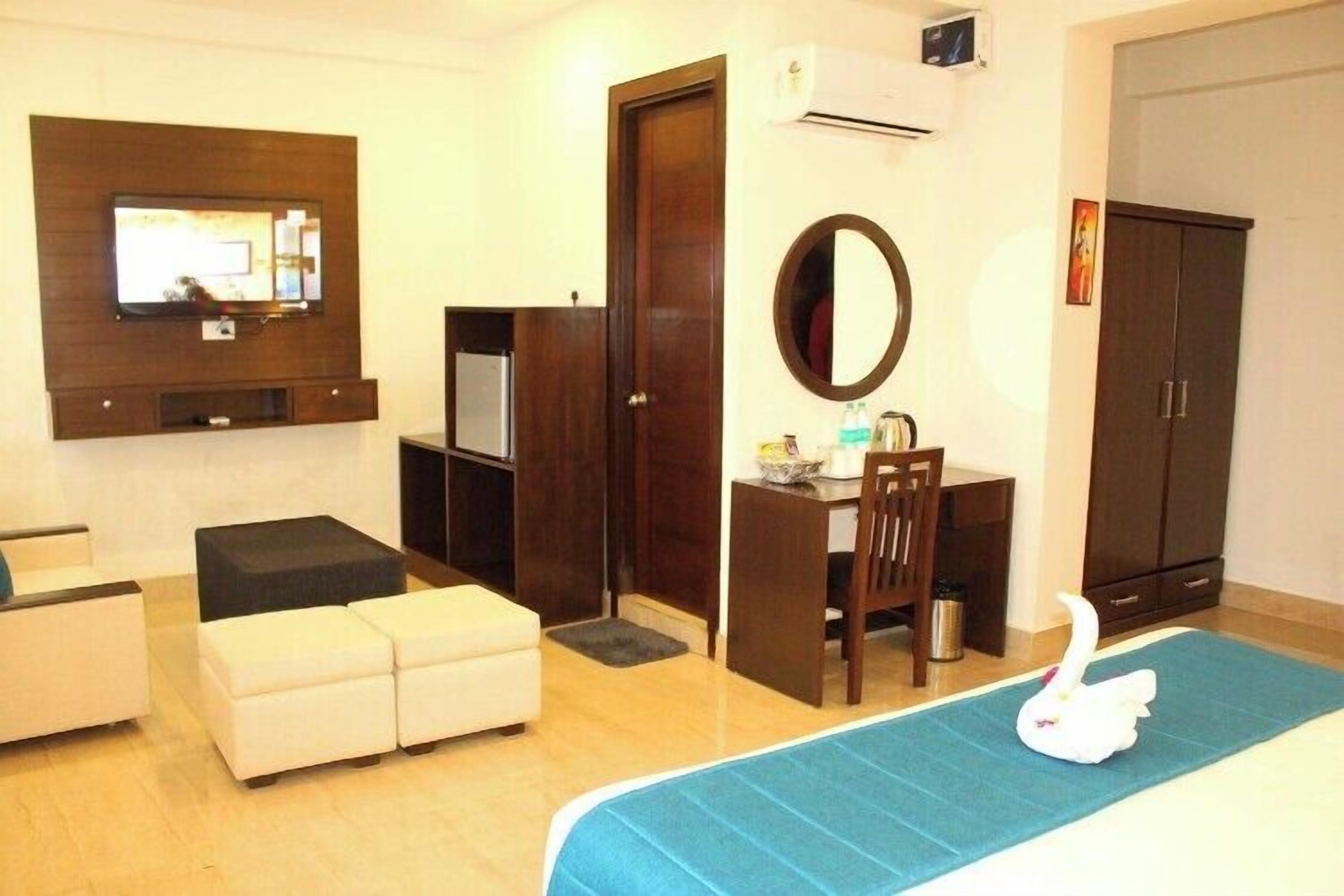 Habitación de hotel con cama, escritorio, silla, televisor montado en la pared, armario y una mesita de noche con espejo.