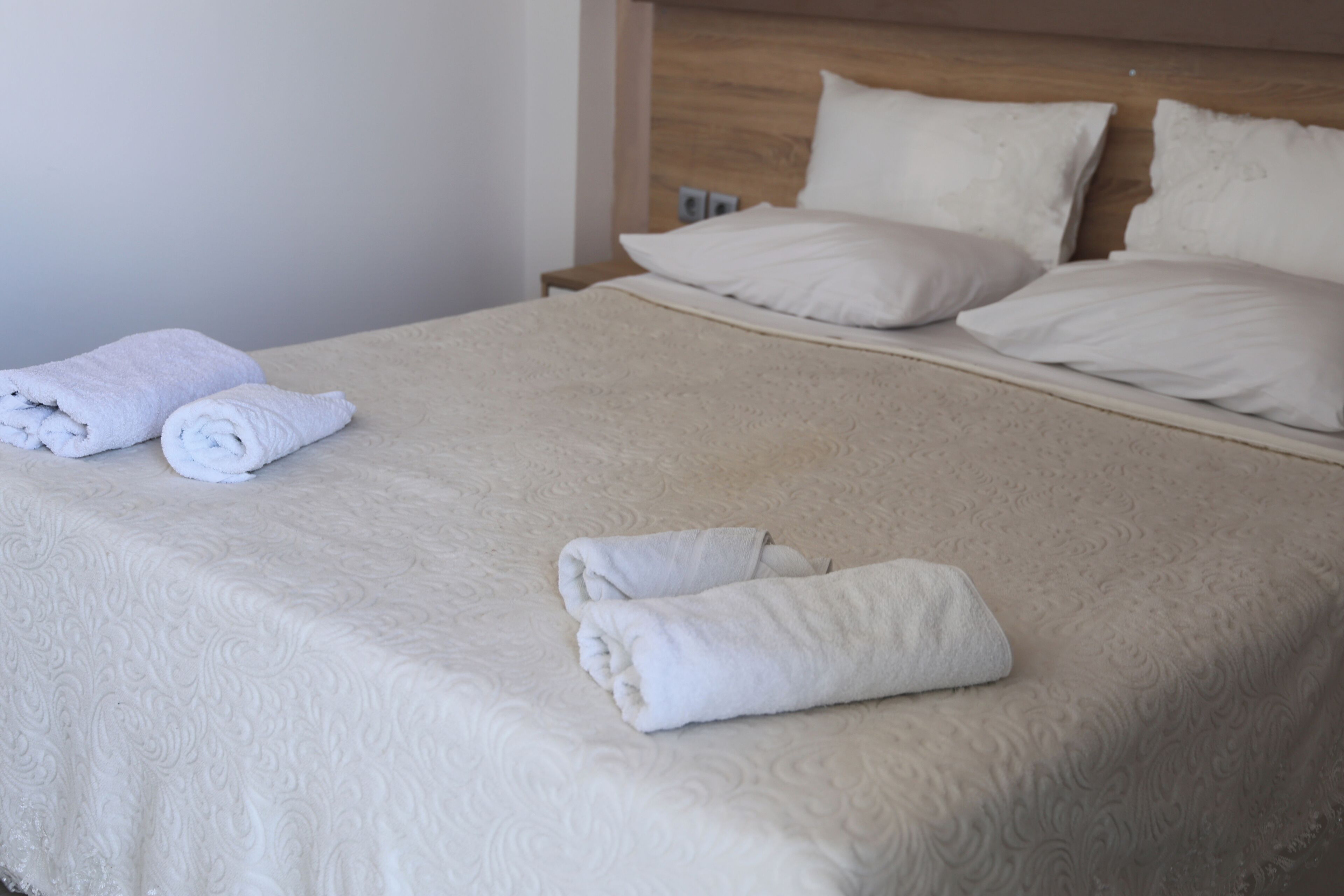 Ein ordentlich bezogenes Bett mit einer beigen Bettdecke, zwei gerollten Handtüchern und einem Holz-Kopfteil.