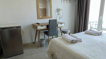 A hotel room with a bed, a desk, a chair, a small fridge, a mirror, a phone, and a window with curtains.
