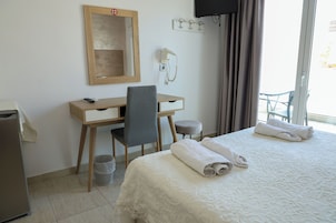 Una habitación de hotel con cama, escritorio, silla, teléfono y un cubo de basura pequeño.