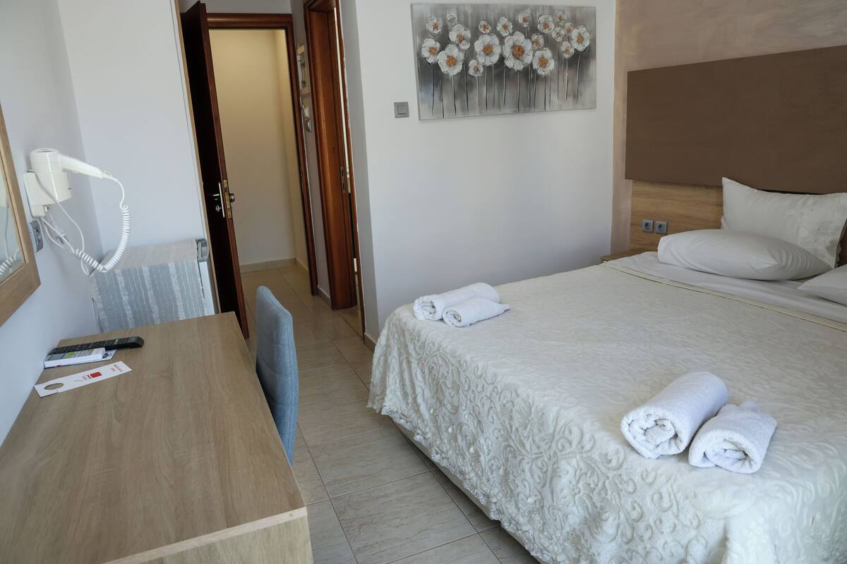 A hotel room with a bed, a desk, a hairdryer, and a painting on the wall.