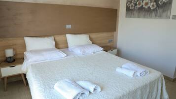 Una cama bien hecha con sábanas blancas y toallas enrolladas, un cabecero de madera y un cuadro en la pared.