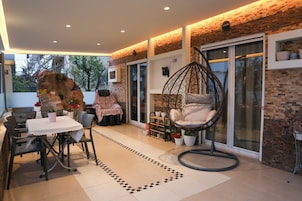 Un patio exterior moderno con zona de comedor, una silla colgante y una pared de ladrillo.