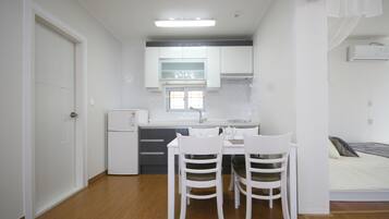 Quarto compacto com cozinha compacta, área de refeições com duas cadeiras, cama e janela.