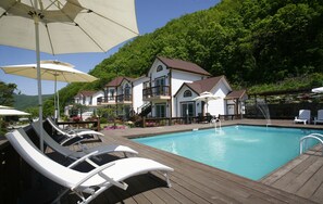 A pool area with lounge chairs and umbrellas, surrounded by a wooden deck and a building with multiple balconies. - Forest of Color Pension (Hongcheon)