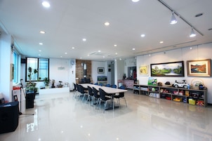 Una habitación amplia con una mesa grande y sillas, una chimenea y una estantería llena de juguetes.