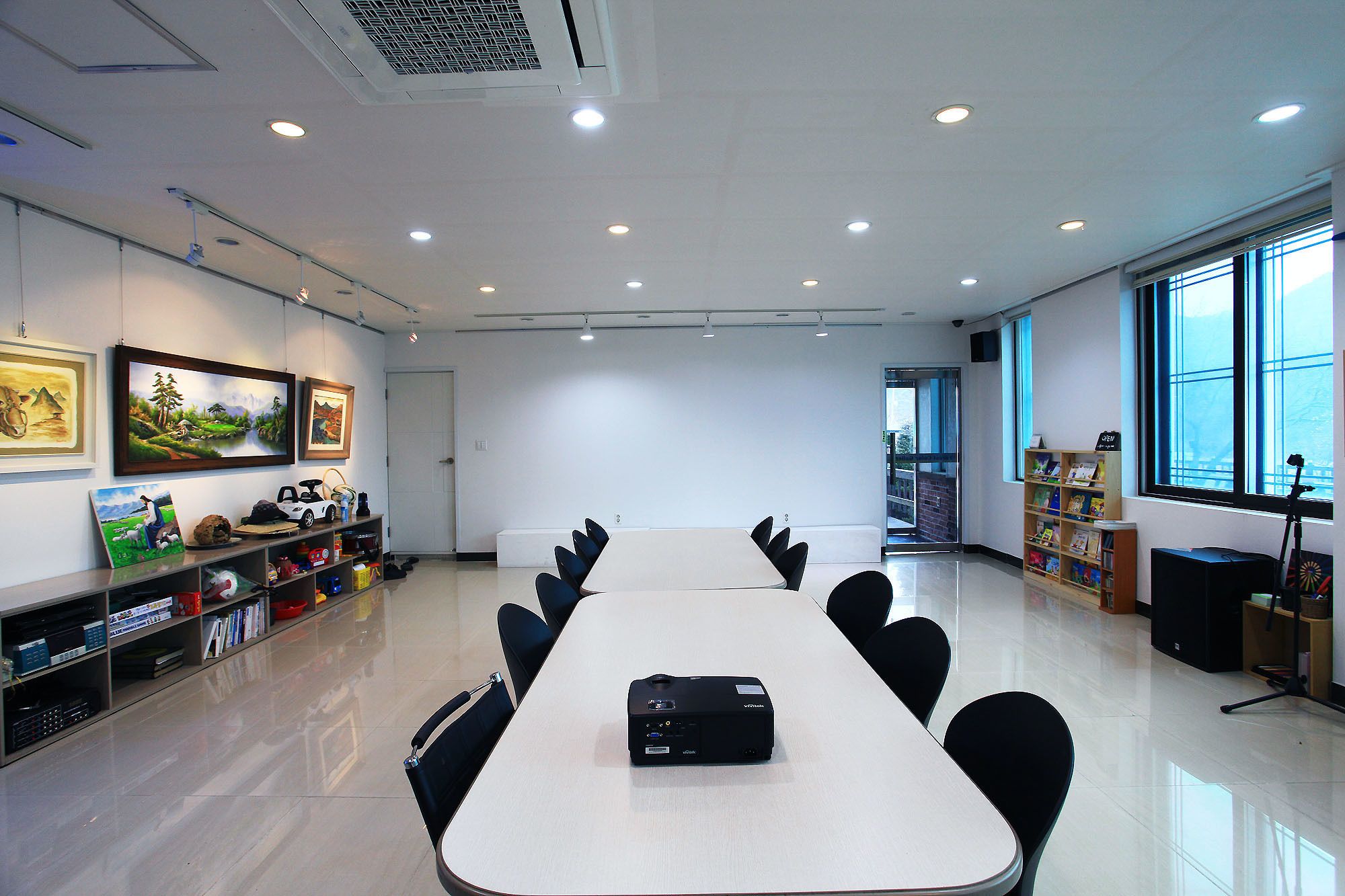 A conference room with a long table, chairs, a projector, and bookshelves with children's books.